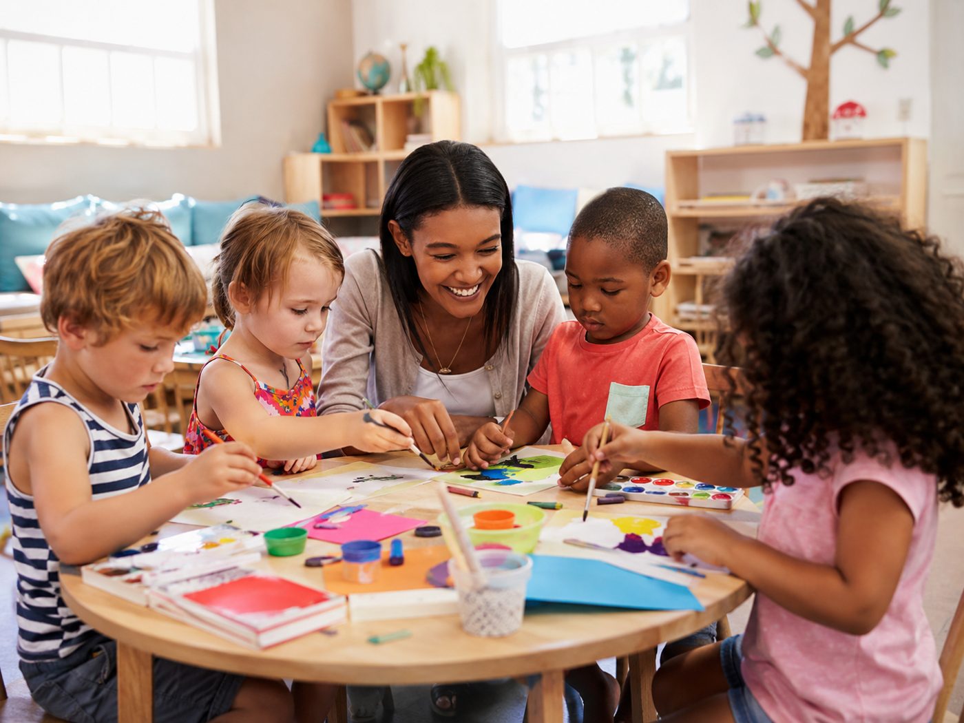 Children painting at an art table with a teacher